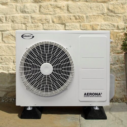 An outdoor heat pump unit mounted on a wall beside a residential building.