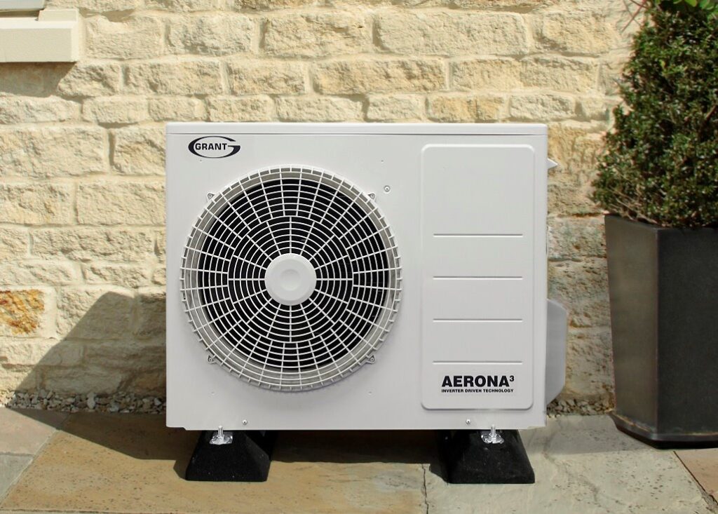 An outdoor heat pump unit mounted on a wall beside a residential building.